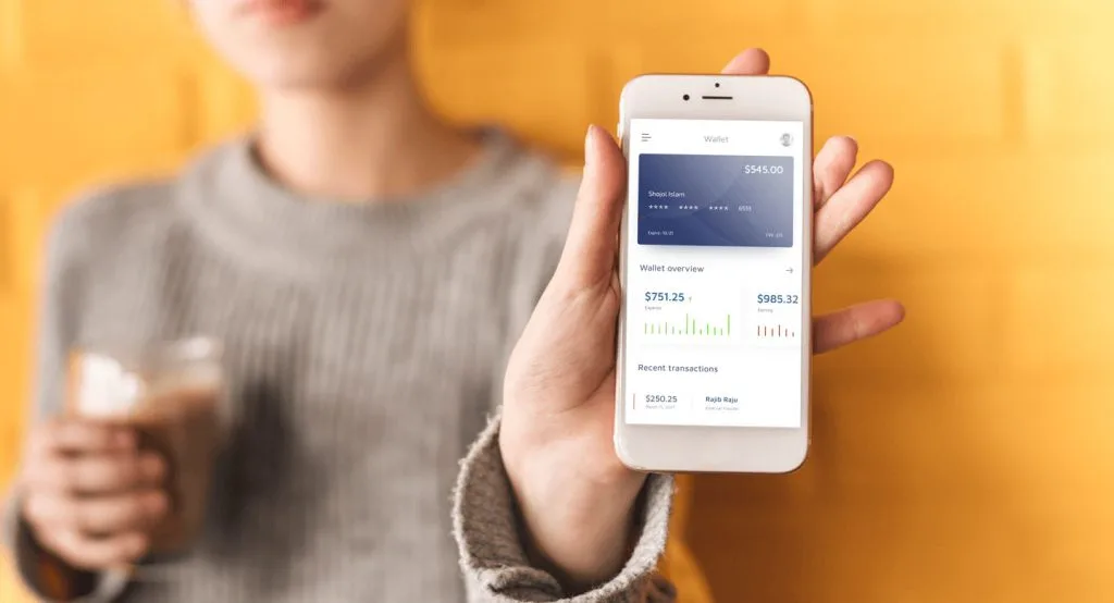 A person holds a smartphone showing a Wallet app screen with a digital card and a Wallet overview bar chart.